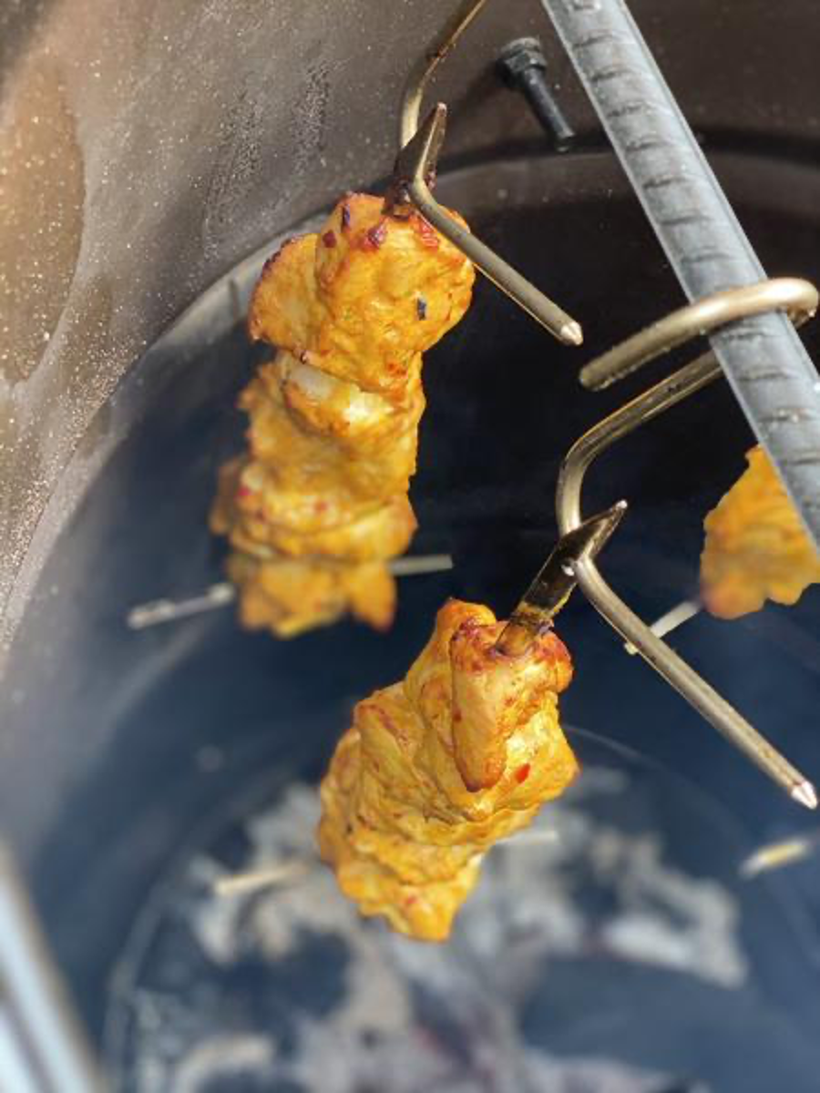 Tandoori Chicken Kebabs Hanging on Skewers in Pit Barrel Cooker