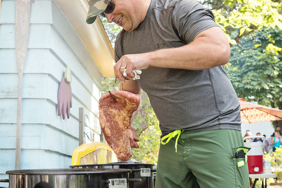 Man grilling meat outdoors near a building with trees in the background